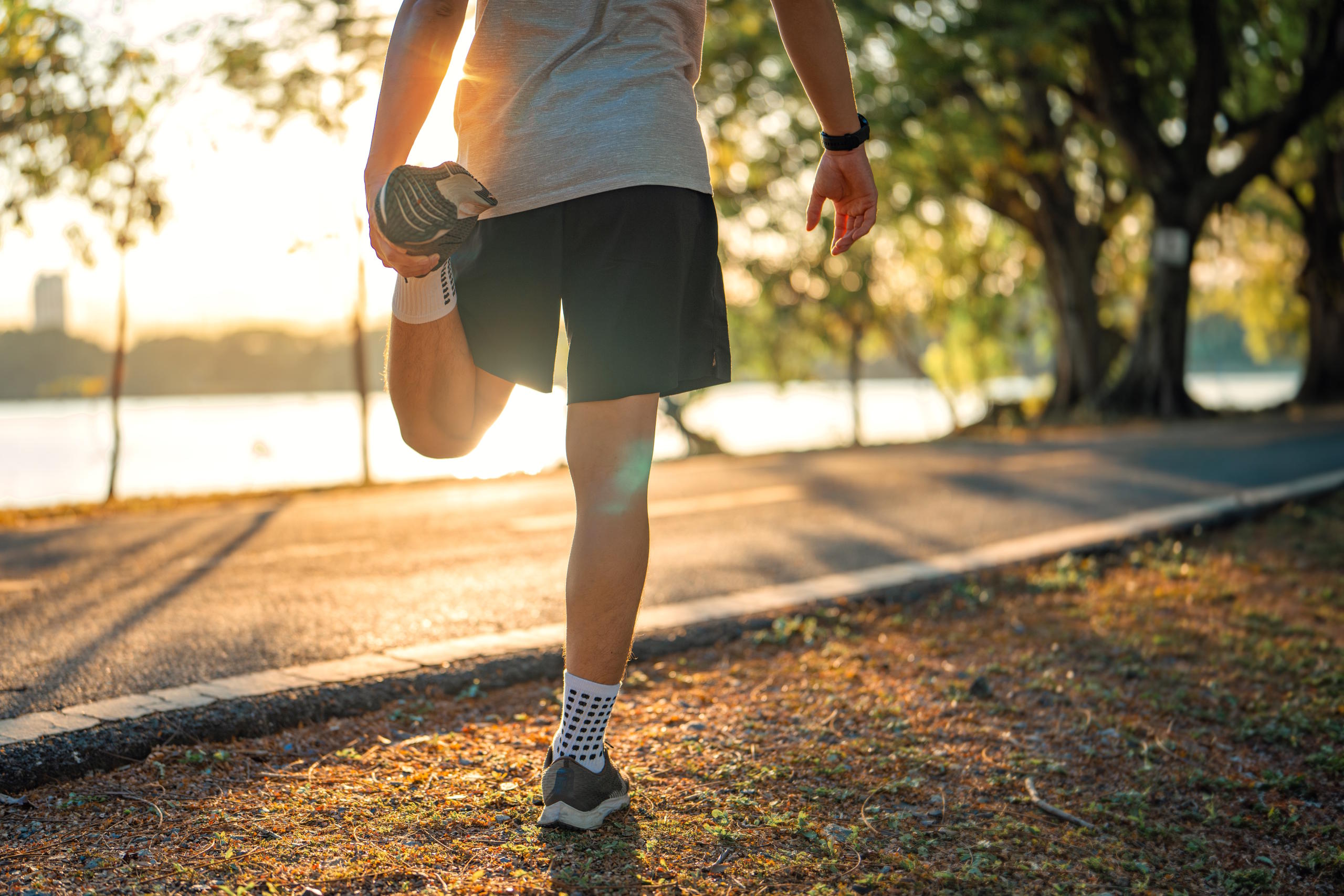 Mann in Laufgewand beim Stretching neben einer Uferpromenade